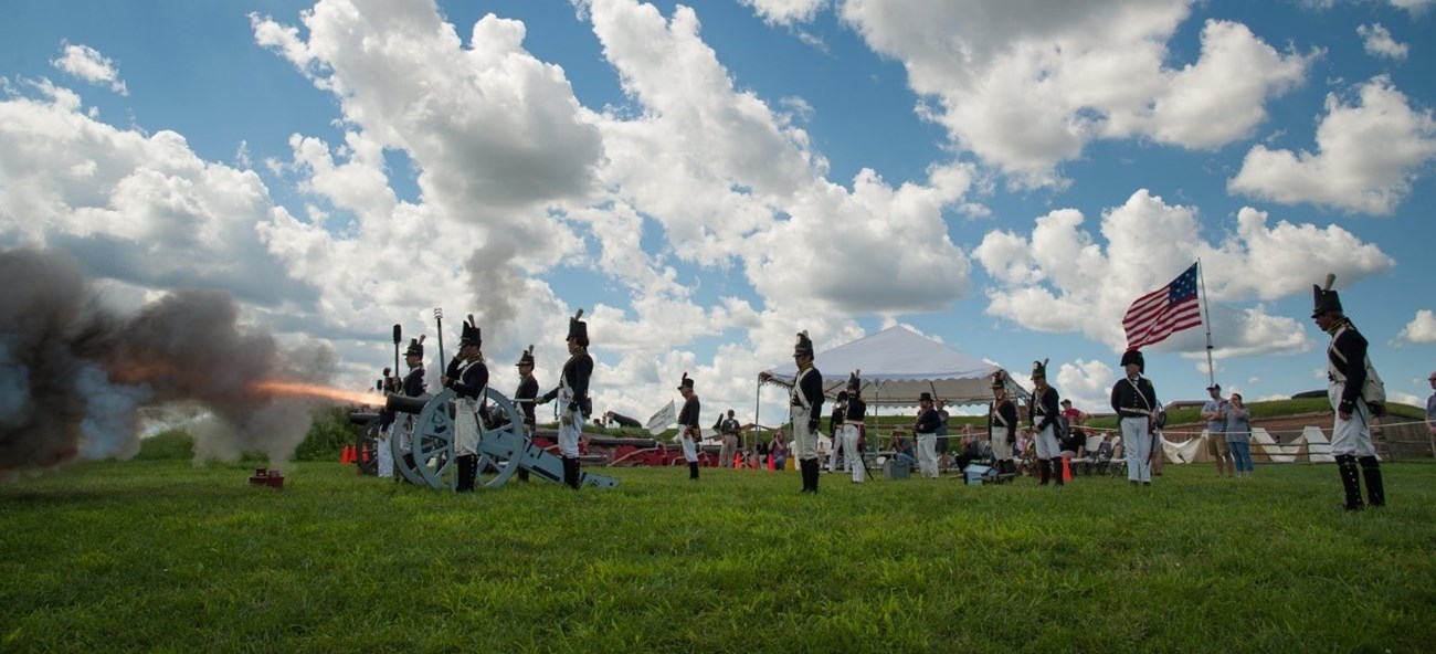 A modern day photograph of living historians dressed as corps of artillery firing a cannon.