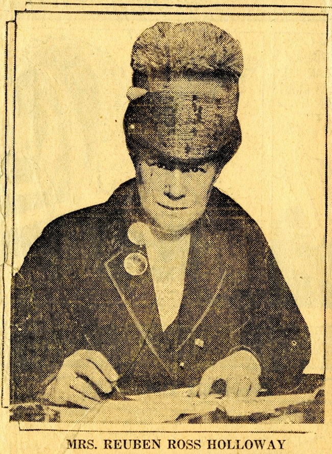A newspaper image of Mrs. Reuben Ross Holloway in a large had signing papers.