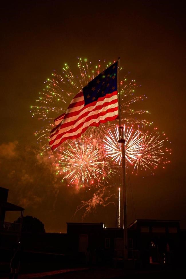 An American Flag waves with fireworks in background.