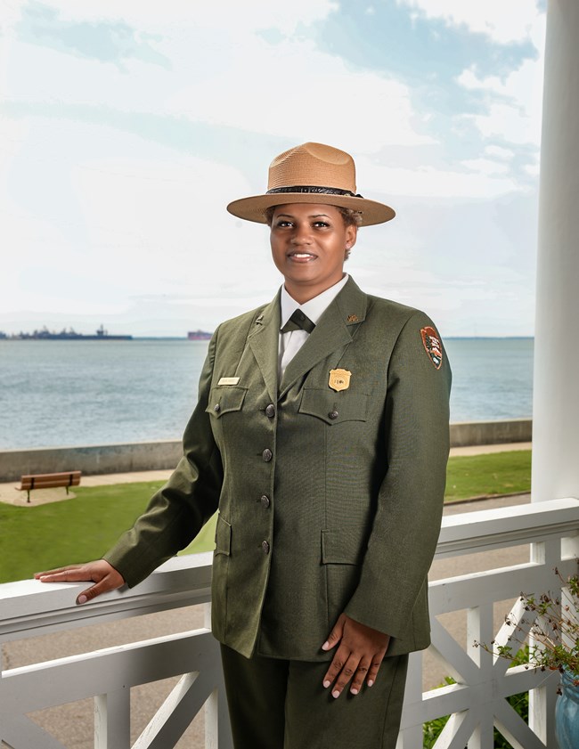 Formal uniform portrait photo on white bandstand with water and Navy ships in the background.