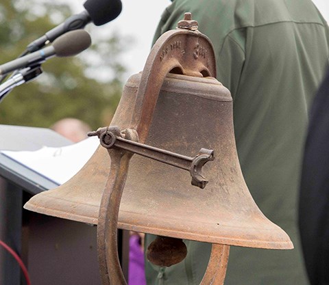 A bell stands on a stage next to a speaker's podium.