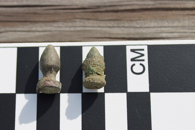 Two small, gray plum bobs about one centimeter long.