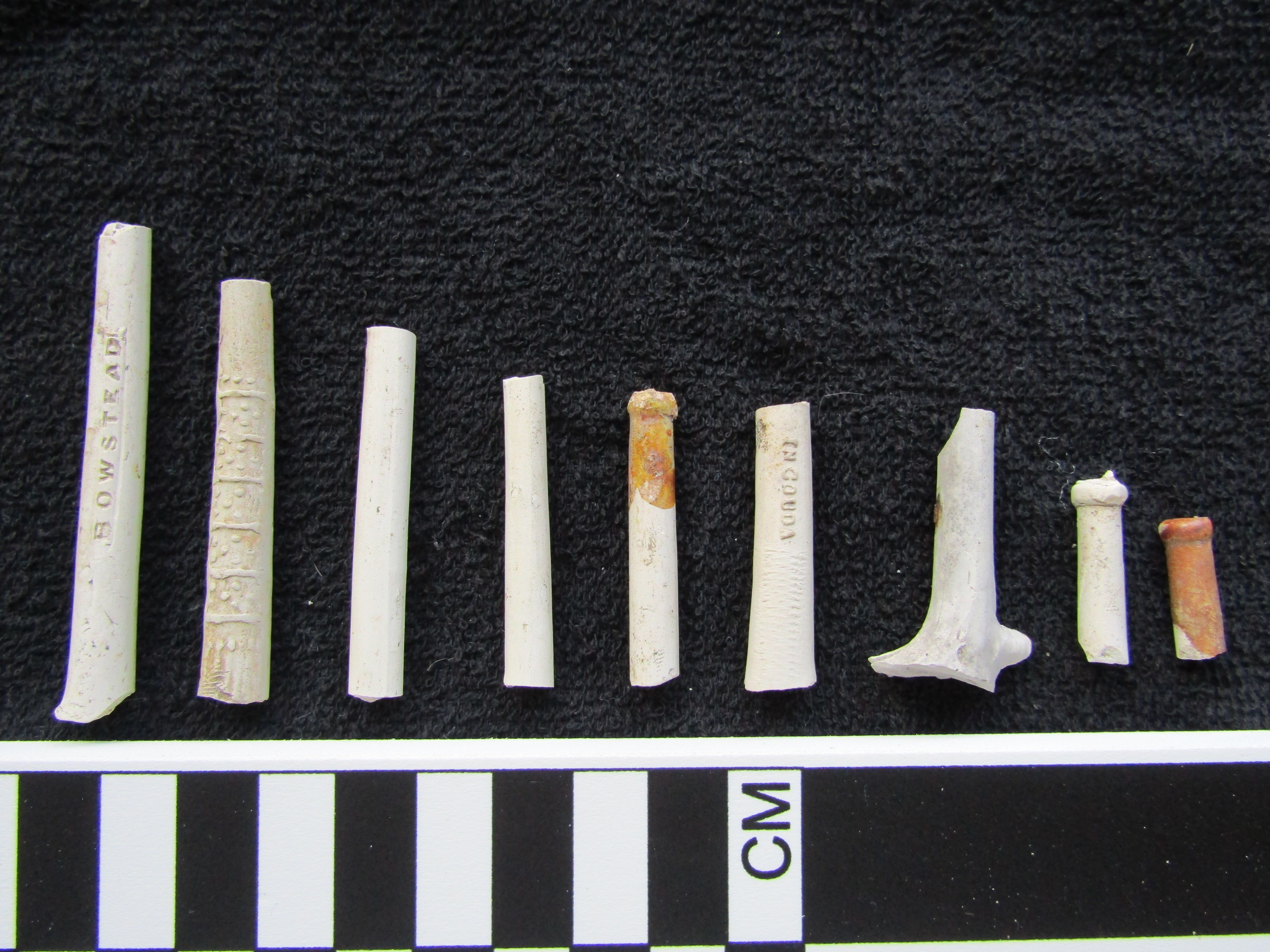 white, cylindrical ceramic pipe stems lined up in a row on a black background.