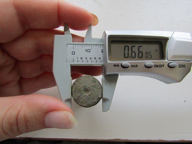 hand holding a caliper with a cartridge case in the tongs.