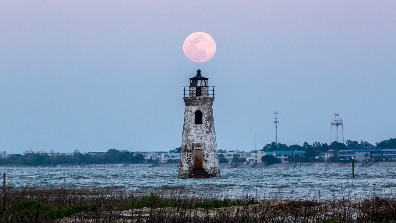 A full moon hovers above the 46 foot tall white painted brick lighthouse.
