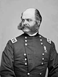 800px-Ambrose_Burnside2. loc A man sitting in a military uniform with sideburns connecting to a large beard