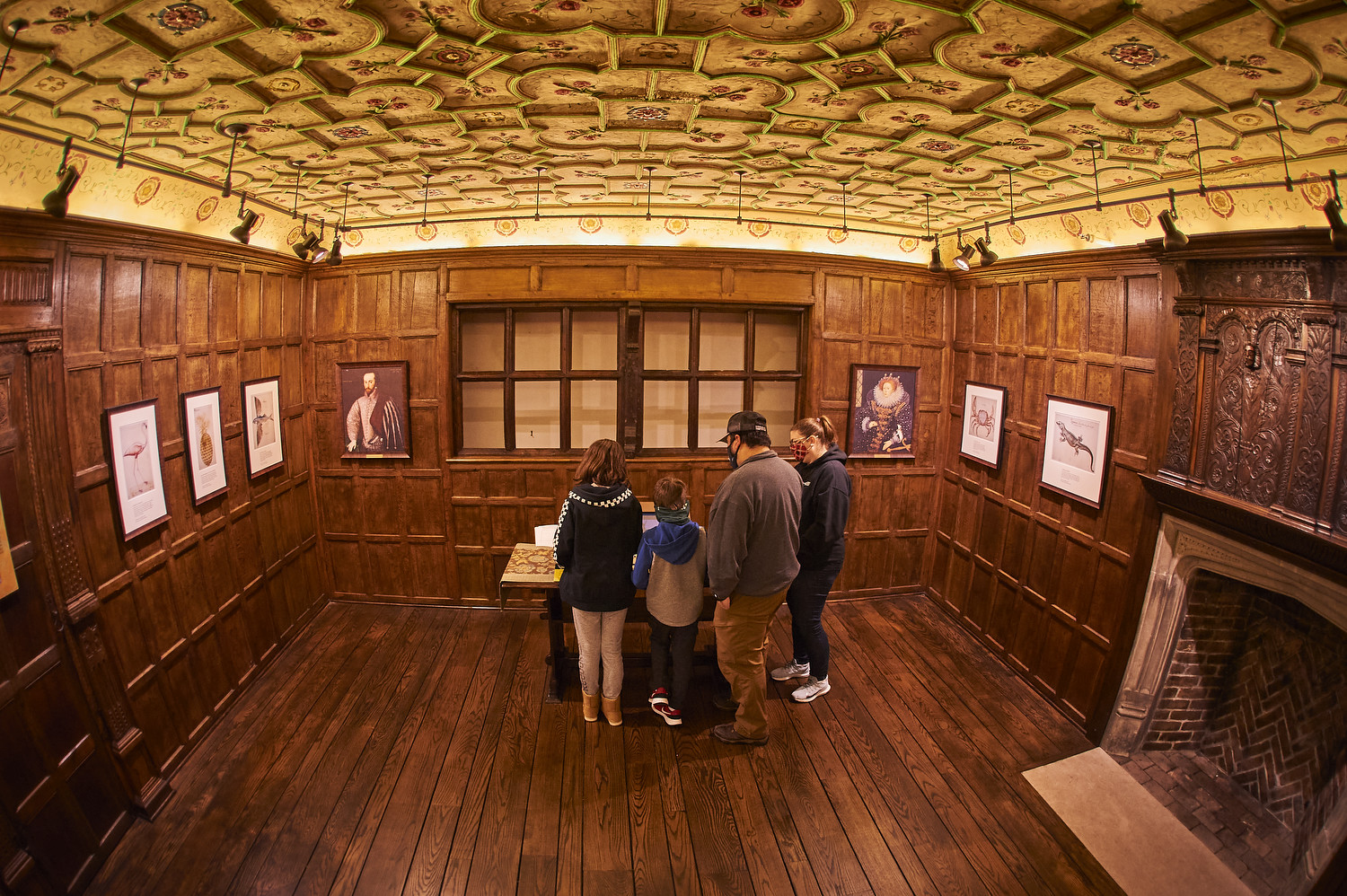 Oak paneled room with plaster ceiling. Family reads exhibit.