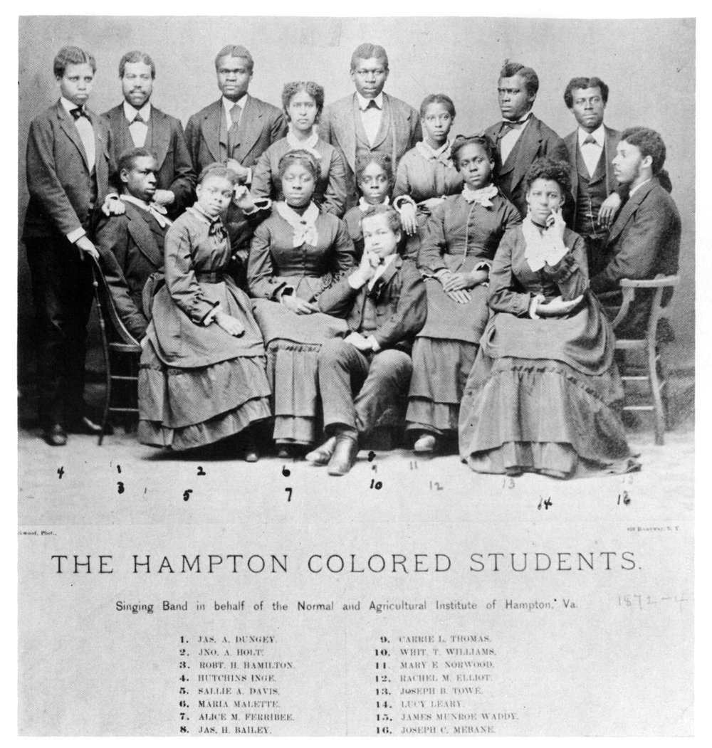A group of Black young adults, some standing, some sitting in formal dress