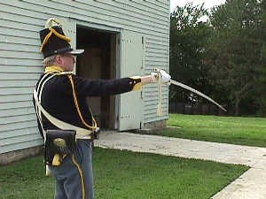 Dragoon in uniform points his saber outside the stables at Fort Scott