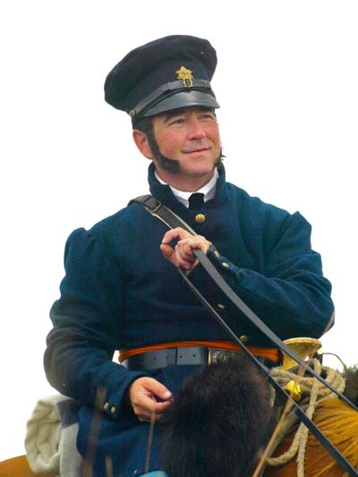 Photo shows a man in blue uniform riding on a horse.