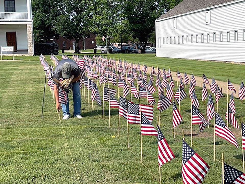 2023 SOS event set up Volunteer helping place small American flags in rows to create a Field of Honor.