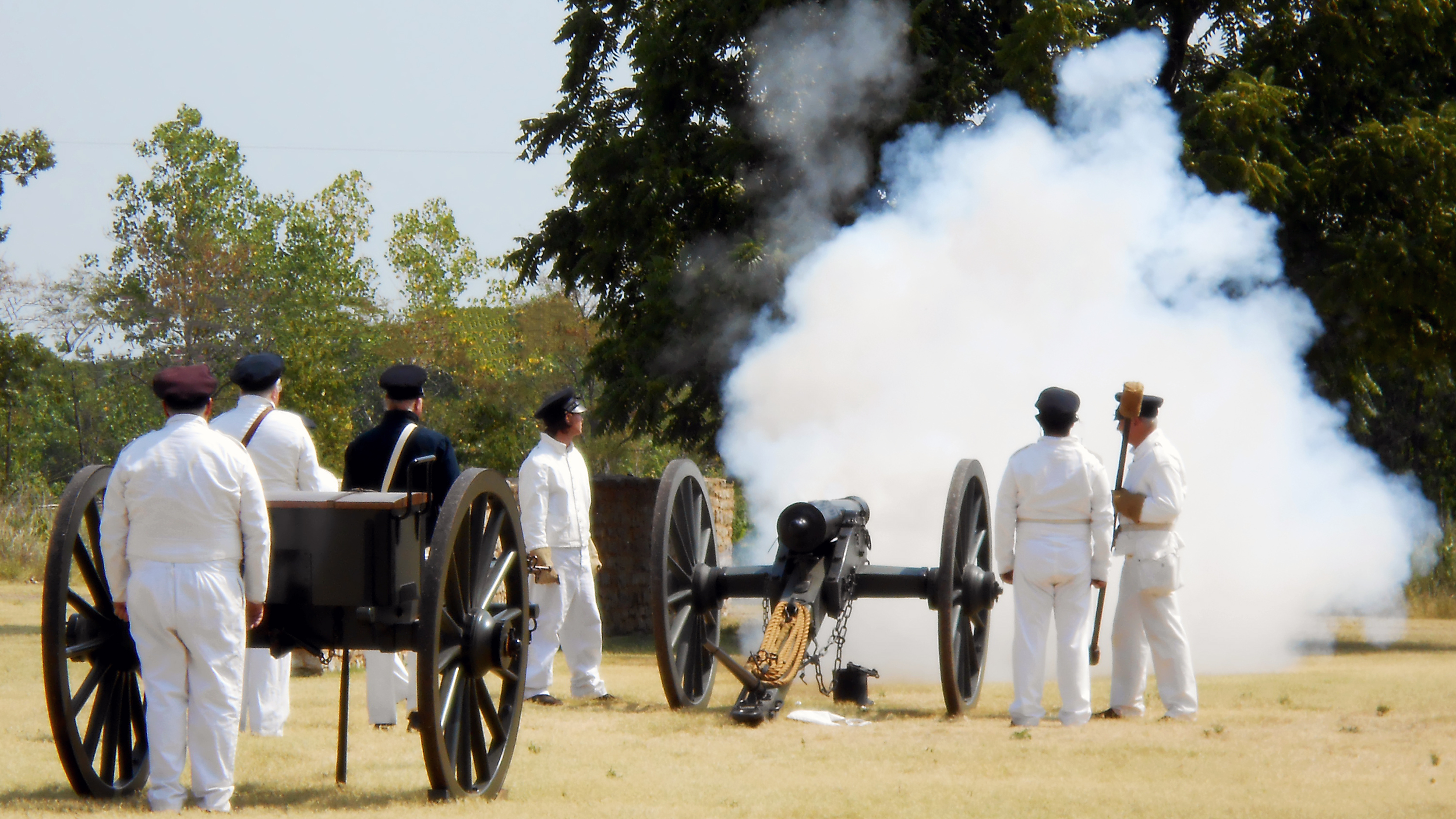 A crew of volunteers dressed in 1840s white uniforms firing a 6lb field cannon.
