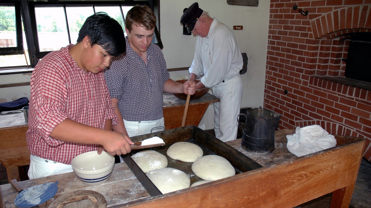 Three men dressed in infantry uniforms preparing bread in the bakehouse.