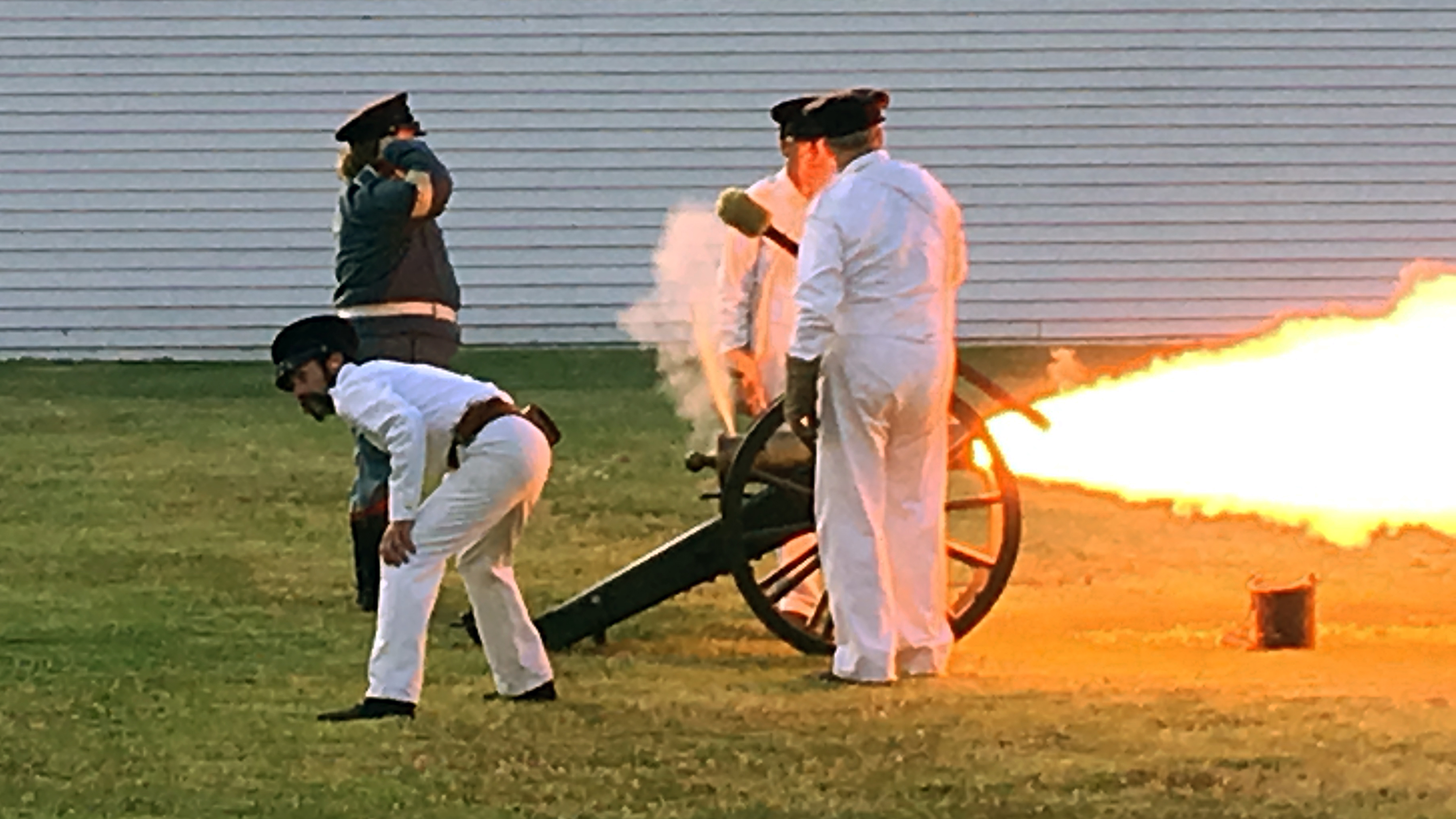 Reenactors, dressed in 1840's military uniforms, firing a 6# cannon.
