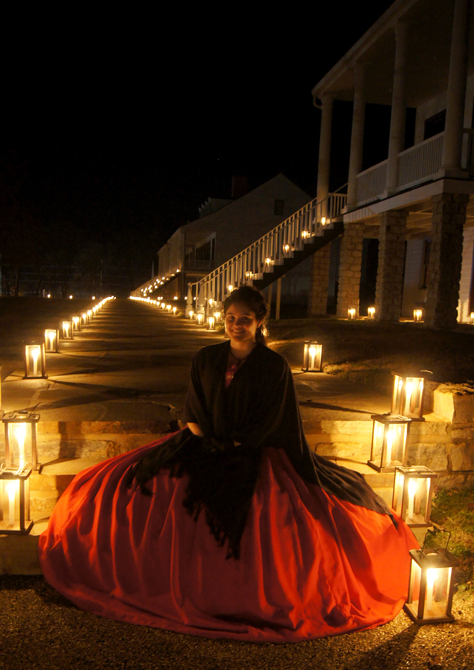 Girl in a red dress sitting on a candlelight walkway's stairs.