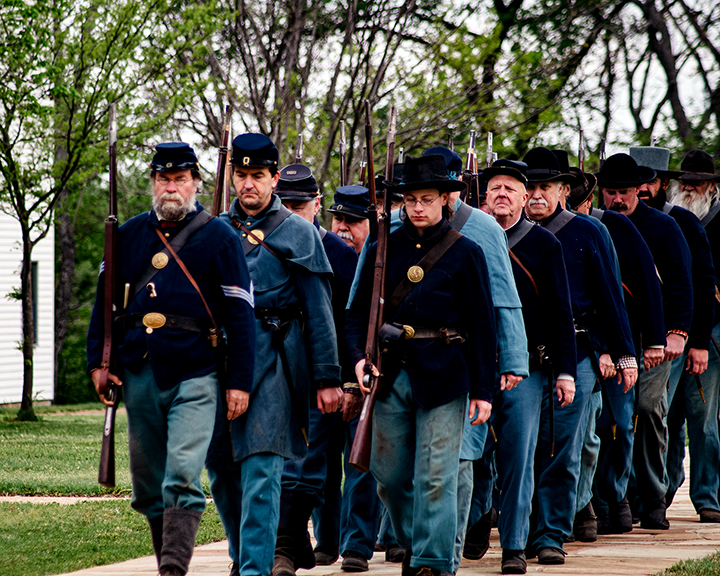 group of reenactors marching in two lines, dressed in blue Union Army uniforms.