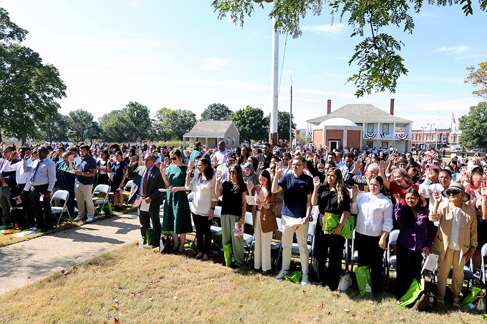 199 New Citizens standing and taking their oath on the grassy parade ground.