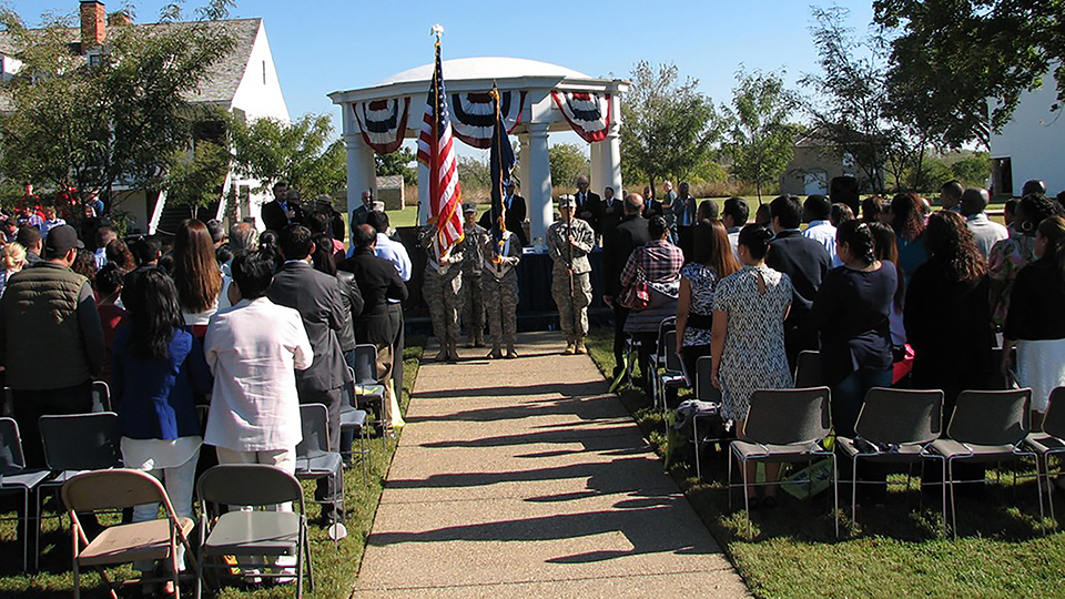 Fort Scott Naturalization Ceremony View toward stage at naturalization ceremony. New citizens on the side, color guard in the center, well canopy and trees in the background.