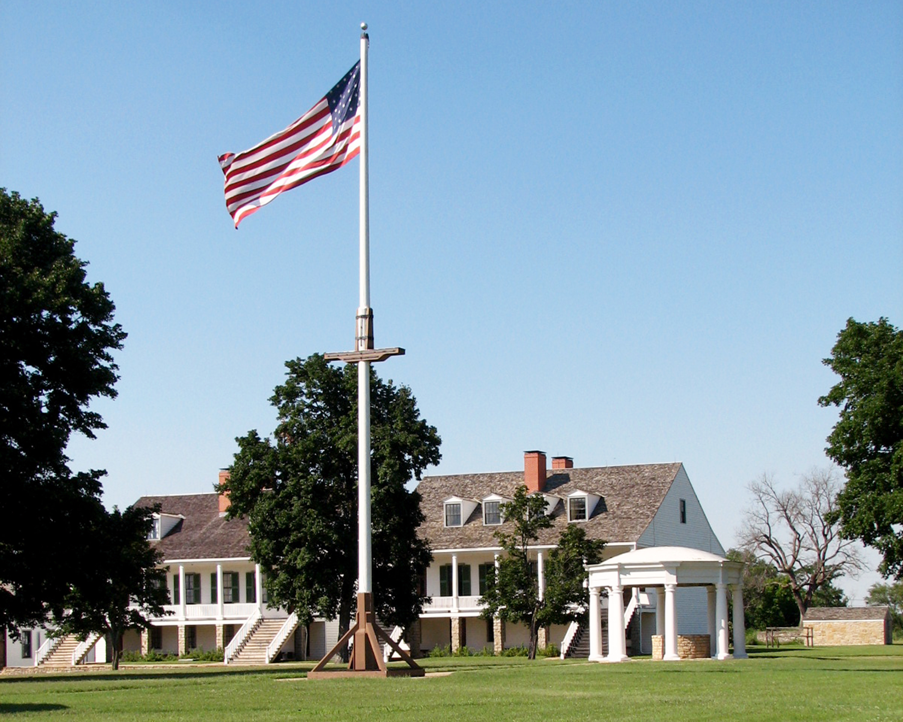 Picture of Fort Scott's parade ground with historic white buildings in the background and the 1848 American flag flying on the flagpole in the center.