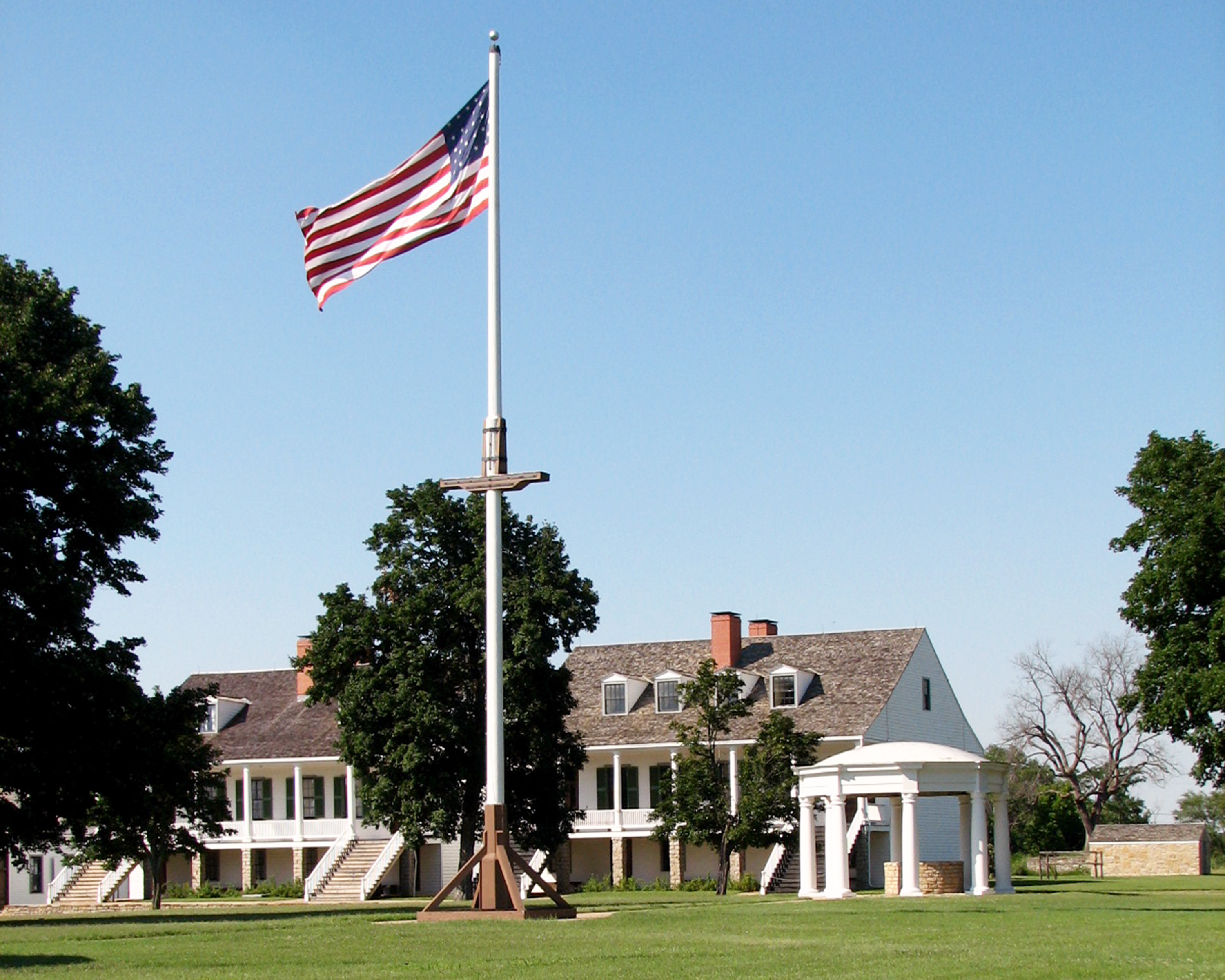 Fort Scott Parade ground Picture of Fort Scott's parade ground with historic white buildings in the background and the 1848 American flag flying on the flagpole in the center.