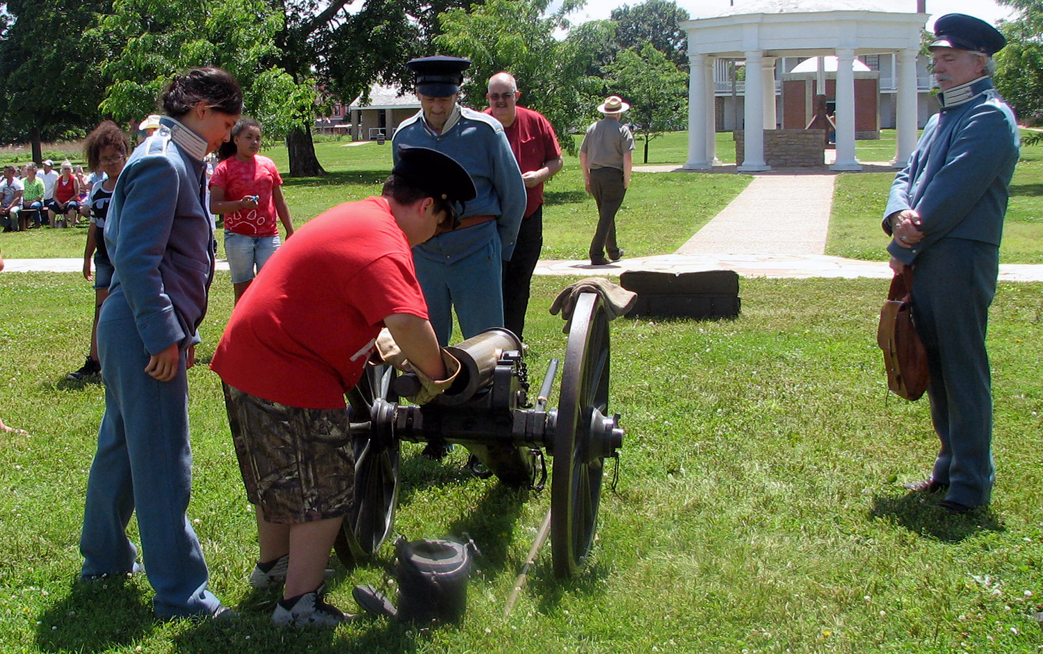 A student helps clean a cannon while three reenactors observe. A student helps clean a cannon while three reenactors observe.