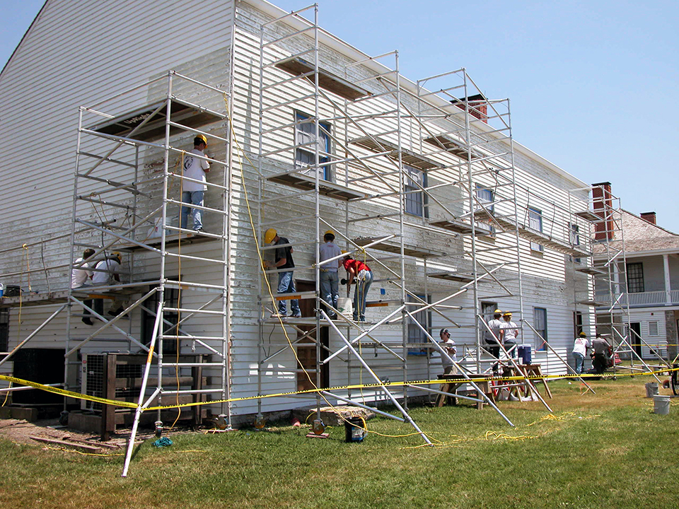 Crew of student interns on scaffolding working on army barracks.