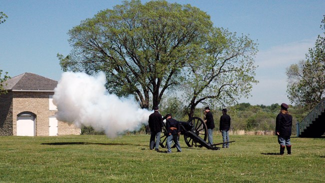 Smoke coming from the barrel during Civil War Encampment cannon firing. Five reenactors dressed in blue uniforms are firing the cannon.