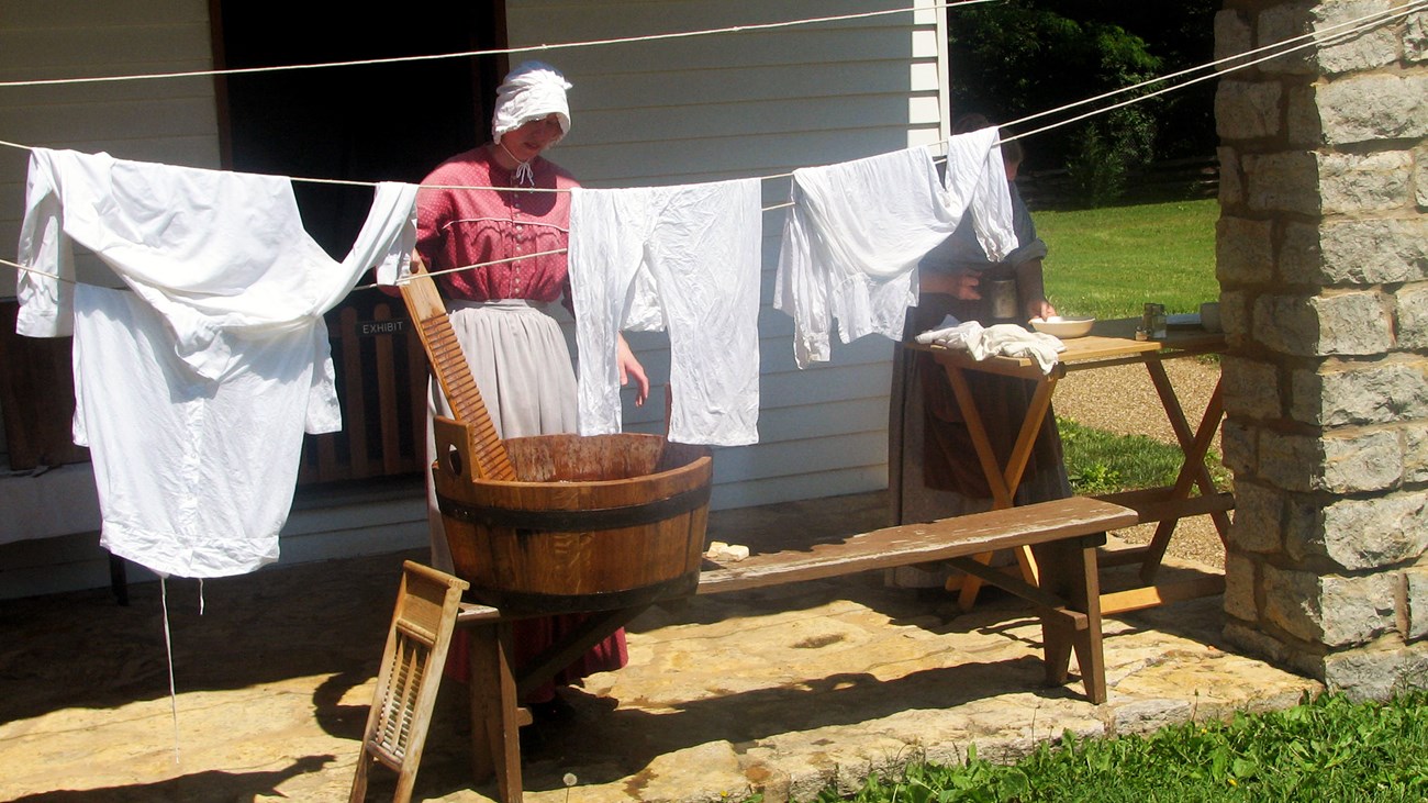 A female volunteer dressed as a laundress hanging laundry on a clothes line.