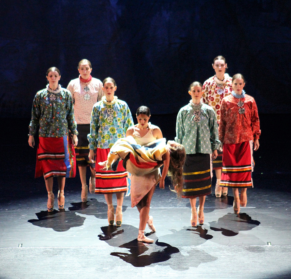 Nine female Osage dancers in traditional regalia with one holding her lifeless daughter.