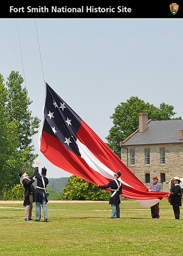 Five Arkansas State Militia members raise the Stars and Bars Confederate flag at Fort Smith with the commissary in the background
