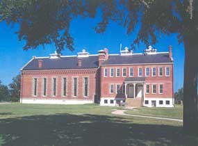 Park visitor center, two story red brick building with slate gray roof as seen from the shadow of tree on a clear sunny day.