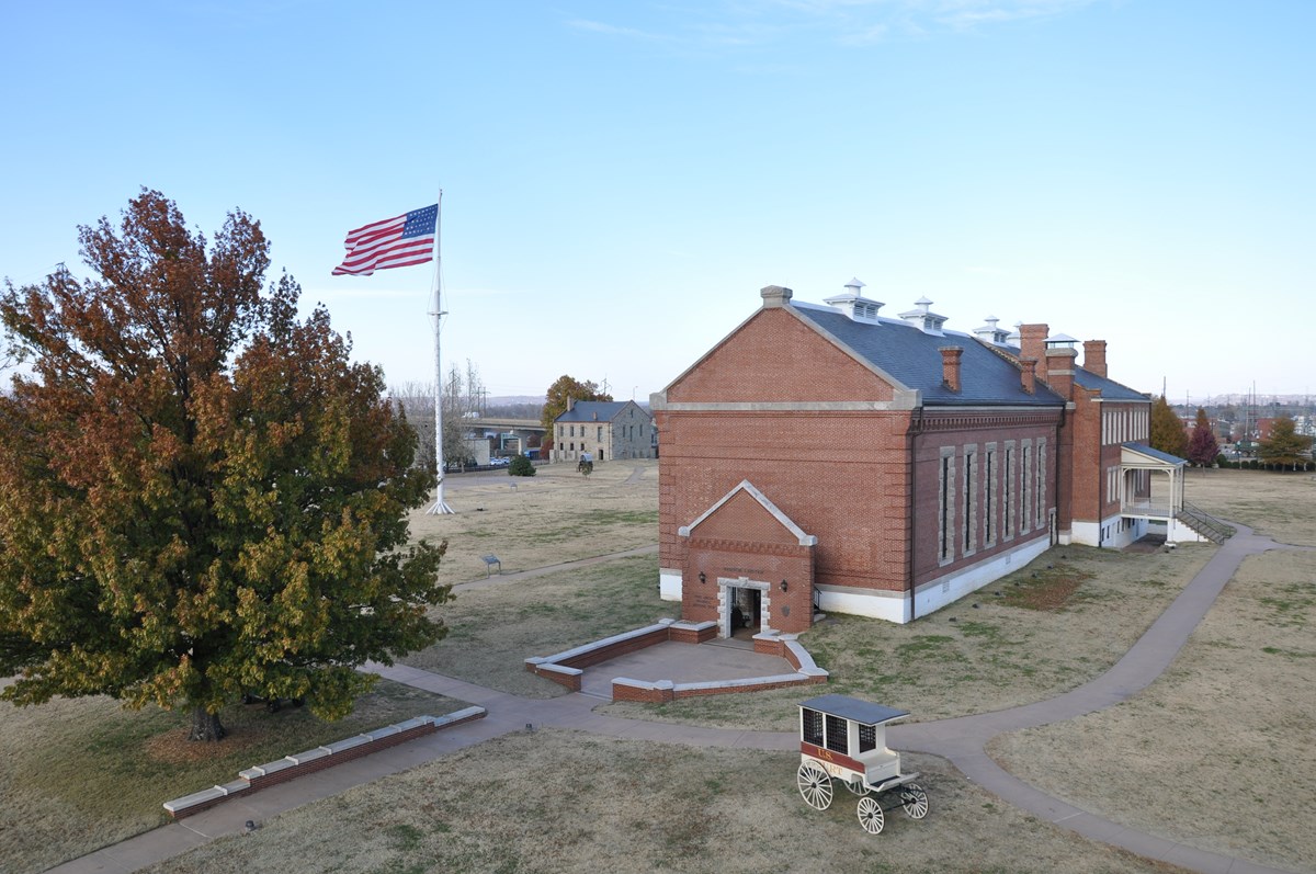 Aerial view visitor center entrance, jail wagon, garrison flag flying over the parade ground, and commissary in background