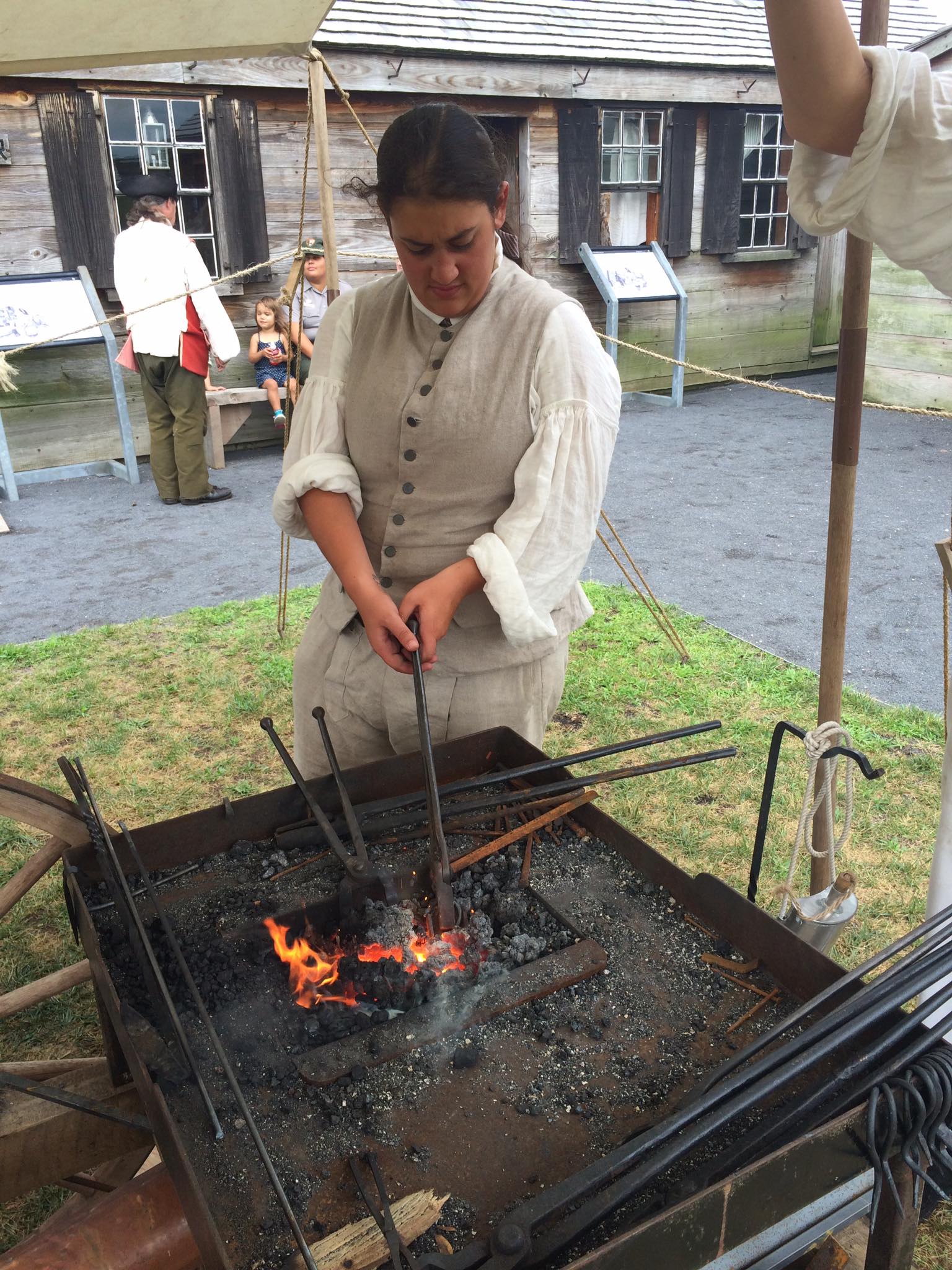 A blacksmith holds iron rods over red-hot coals.