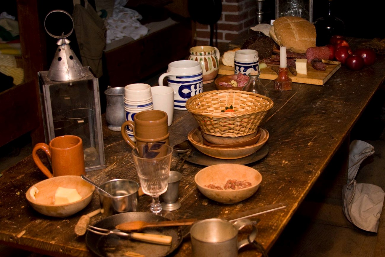 A wooden table with various ceramic, wooden, and metal plates, bowls, and cups strewn about the top.