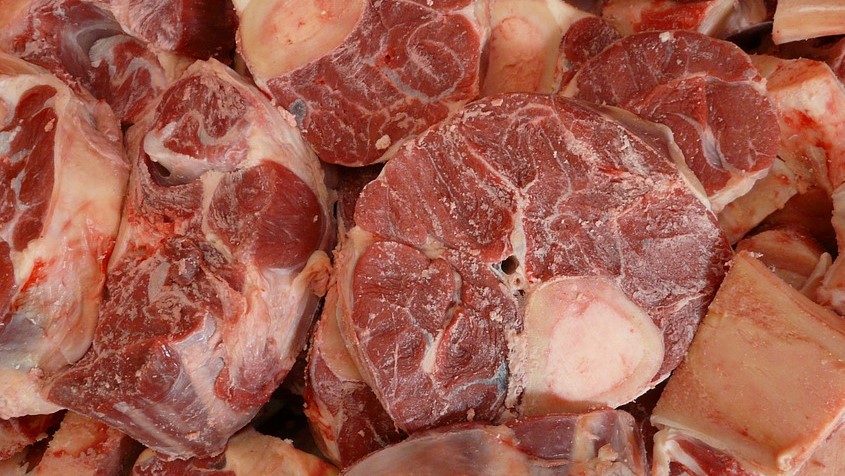 Chunks of raw red beef and bone in a pile.