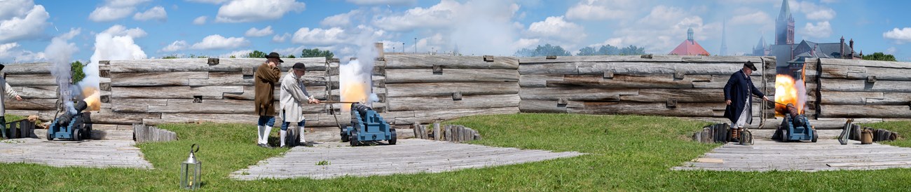 Three cannons are lined up in front of you, facing out of the fort wall. They are surrounded by flashes of smoke and fire.