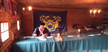  A New York State flag on a wall that has ladies liberty and justice on it. An officer table sits in front of the wall.