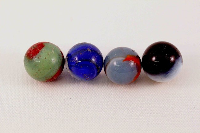 Four colorful glass spheres, about the size of a walnut, sit in a row.