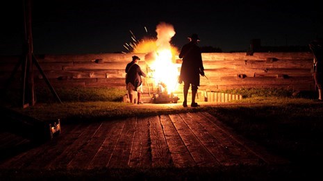 A dark pitch dark photo, two soldiers are illuminated by a ball of fire from a cannon muzzle.