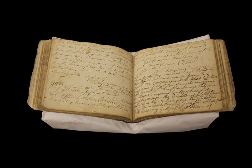A photo of an old tattered book opened to the center. Faded cursive handwriting is across the pages.