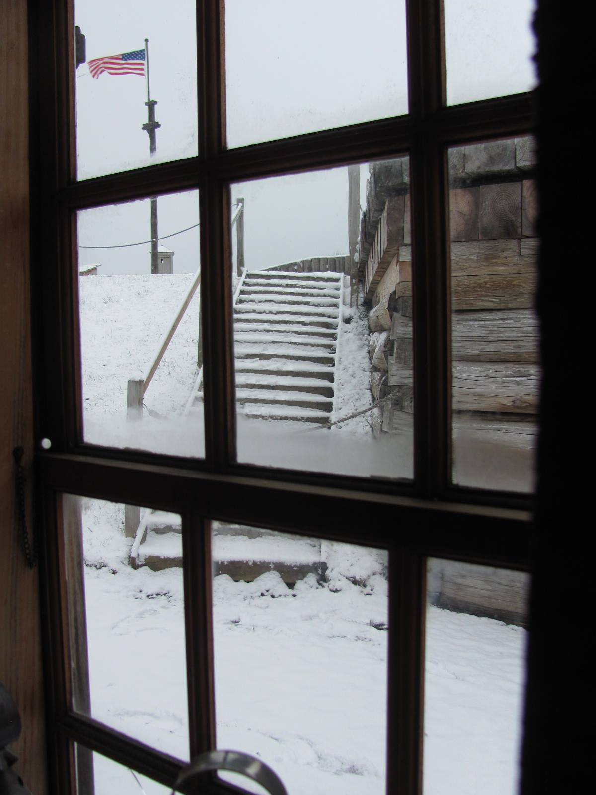 A view of snowy stairs through a window pane. An American flag flies at the top of the stairs.