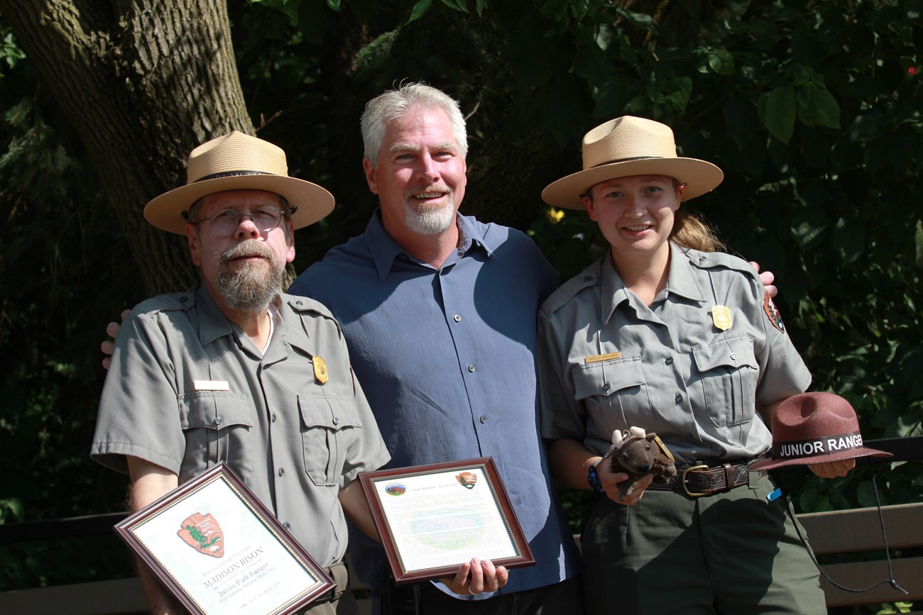 Three people stand in a line. Two are park rangers. They hold frames.