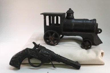 A rusty toy pop-gun and locomotive sit on a clean cushion.