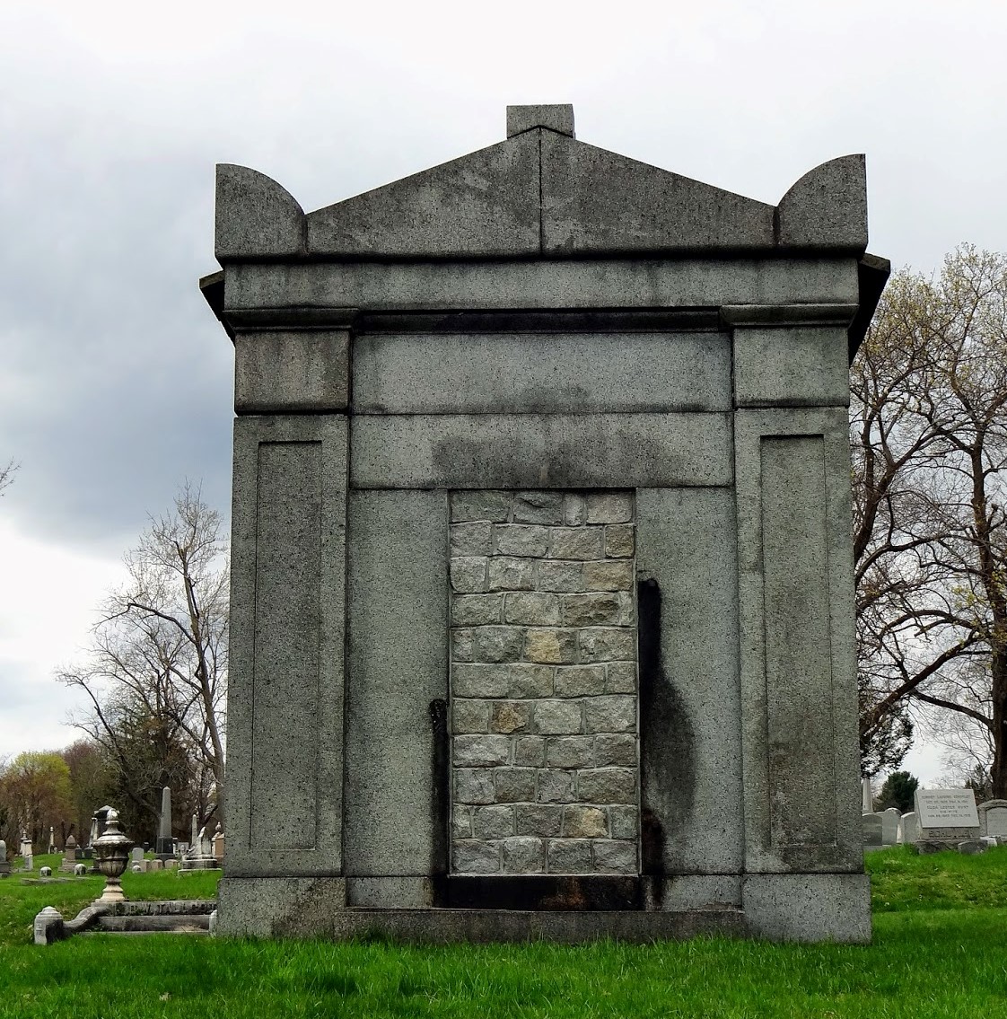 A small stone building with no windows. The door is sealed closed with rough hewn bricks.. 