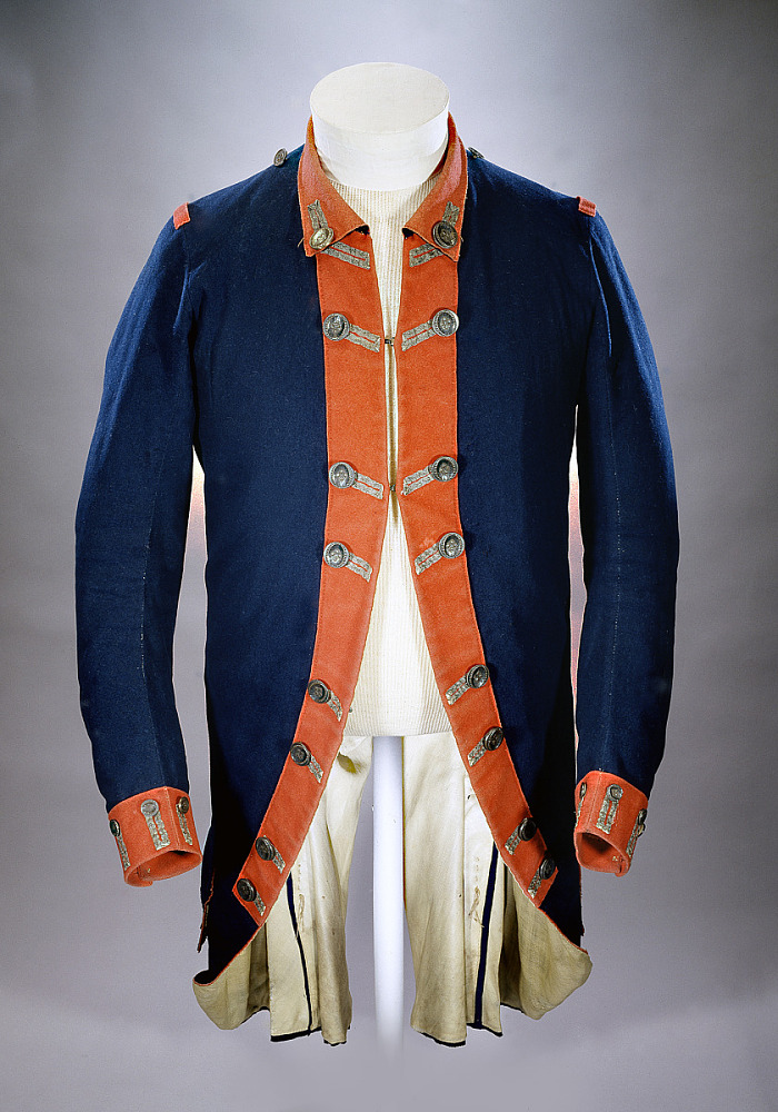 Superfine blue wool, lined with linen and faced with red trim. It has silver civilian patterned buttons backed with bone and a silver lace on the buttonholes.