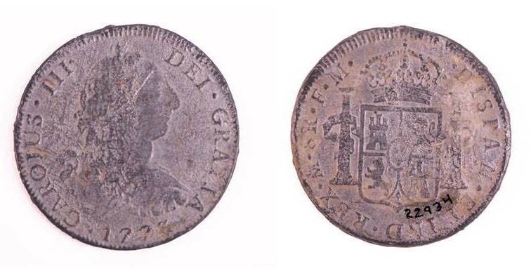 Front and back of a smooth, silvery coin. A shield on one side and a face in profile on the other.