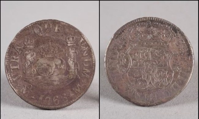 Front and back of a darkened, pitted coin about the size of a quarter.