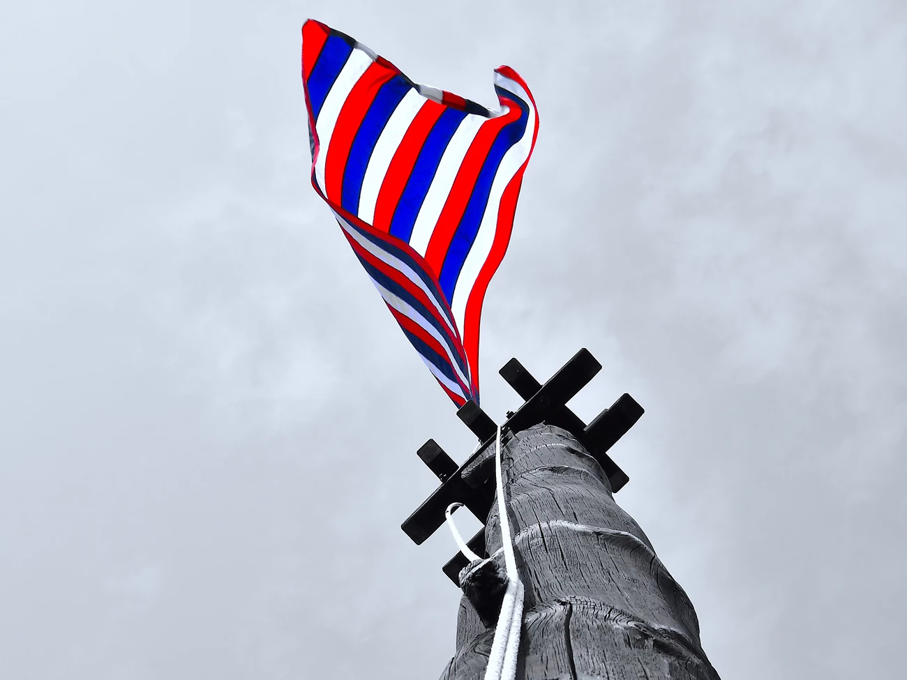 siege flag splash_00002.crop Looking up a wooden ship's mast-like pole, a pop of color and a red, white, and blue flag flutters at the top, over your head.