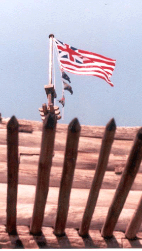 A flag with the British Union Jack in the top right corner and red and white stripes flies at the top of the pole. Under it are multicolored regimental flags fluttering. They can only be seen lighted from the bottom through the outside fort walls and pickets. A flag with the British Union Jack in the top right corner and red and white stripes flies at the top of the pole. Under it are multicolored regimental flags fluttering. They can only be seen lighted from the bottom through the outside fort walls and pickets.