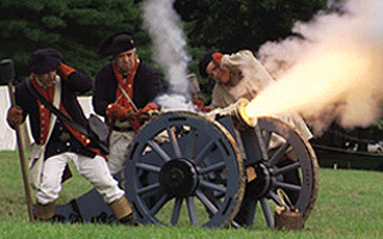 men stand near a smoking howitzer with sparks and fire spewing from the muzzel